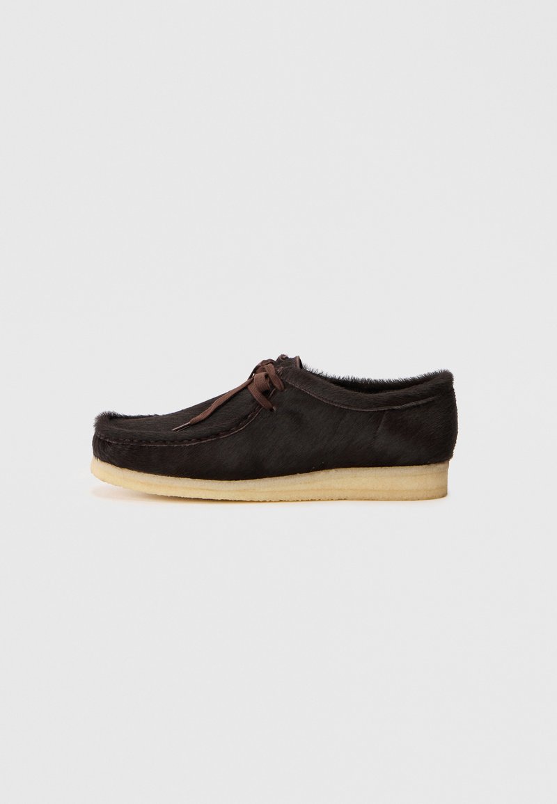 Brown leather moccasin shoe with a soft texture, featuring a lace detail, rounded toe, and a light-colored rubber sole.