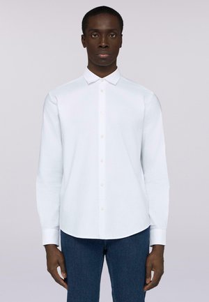 Chemise blanche à manches longues avec un col pointu. Réalisée en tissu doux, elle présente un ourlet arrondi et un design uni. Portée avec un jean foncé.