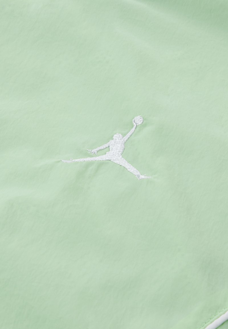 Tessuto verde chiaro con un logo Jumpman ricamato in bianco. Il materiale sembra liscio con una texturizzazione minimale.