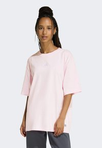 Svijetloružičasta oversized majica od pamuka, s malim ljubičastim logotipom na prsima i kratkim rukavima. Mekana tekstura, jednostavan dizajn.