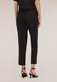 Zwarte broek met een rechte pasvorm en opgerolde manchetten, gemaakt van zachte stof. In combinatie met zwarte sandalen met hoge hakken en bandjes.