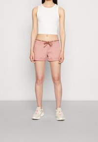 Pink shorts with a drawstring waistband and brown accents, paired with a white sleeveless top and light-colored athletic shoes.