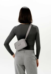 Šedá krosbody taška s hladkým povrchem, obdélníkovým tvarem a nastavitelným popruhem; obsahuje decentní logo a zipové uzavření.
