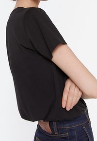 Sort kortærmet skjorte med en afslappet pasform, blødt stof, rund halsudskæring og diskrete sømdetaljer, parret med denim jeans.