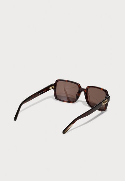 Brown tortoiseshell sunglasses with rectangular frames, semi-transparent lenses, and gold accents on the temples featuring "GCOS" branding.
