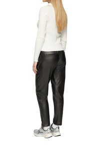 Witte geribbelde gebreide trui gecombineerd met zwarte leren broek en grijze sportschoenen. De outfit toont een aansluitend ontwerp met subtiele accenten.