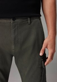Olivgrüne Cargo-Hosen aus Baumwollmischgewebe, mit Knopfverschluss, Seitentasche und geradem Schnitt.