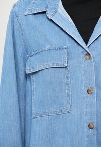 Helles, blaues Jeanshemd mit Kragen, Brusttasche und braunen Knöpfen. Strukturierter Stoff mit lockerer Passform und lässigem Design.