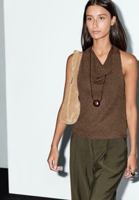 Top senza maniche in maglia marrone con scollo a caramella, abbinato a pantaloni larghi verde oliva e una borsa a spalla in suede beige.