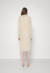 Knälång, ribbad stickad klänning i ljusbeige, med krage och långa ärmar, ihop med beige klackmules.