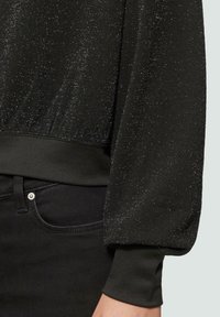 Czarny top wykonany z teksturowanej, metalicznej tkaniny z subtelnymi iskrzącymi się elementami. Dopasowane mankiety i miękka talia uzupełniają projekt.