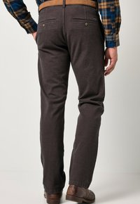 Pantaloni uomo grigio scuro in cotone con una texture liscia, dotati di due tasche posteriori e chiusure con bottone, abbinati a scarpe marroni.
