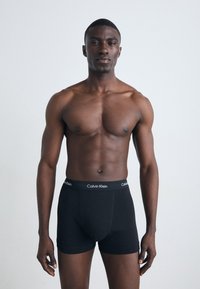 Fekete pamut boxer alsó Calvin Klein logós derékkal, egy sportos testalkatú modellen, sima háttér előtt.
