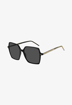 Óculos de sol quadrados oversized pretos com lentes cinzas. Apresentam uma armação de plástico brilhante e finos detalhes metálicos dourados nas hastes.