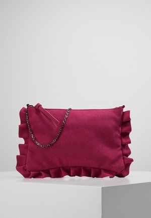 Lille dyb pink ruskind clutch taske med rynkede kanter og en tynd sølvkæde strop, der hviler på en hvid overflade.