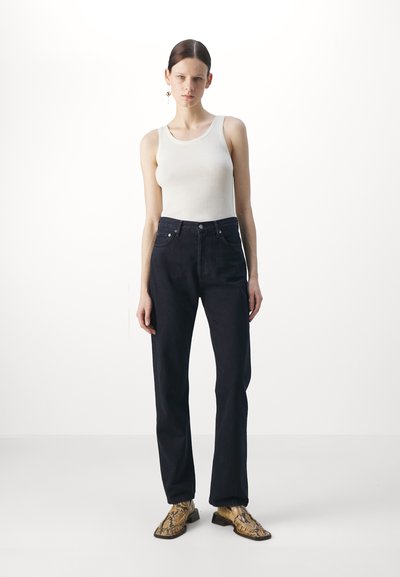 Svarte høye jeans med fem lommer, kombinert med en hvit ribbestrikket tanktopp og gule sko med pytonmønster. Glatt tekstur, tettsittende design.