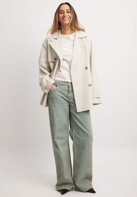 Bežinė dvigubo užsegimo trenčkotė virš baltos palaidinės, derinama su plačiakulkėmis šviesiai mėlynomis džinsomis. Juodi batai su smailiu pirštu užbaigia įvaizdį.