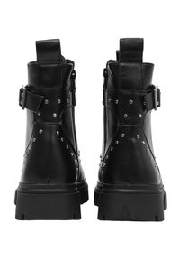 Stivali alla caviglia in pelle nera con borchie metalliche, cinturino regolabile, linguetta posteriore e suola spessa. Chiusura con zip sul lato.