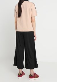 Ljust rosa kortärmad topp med svart krage, ihop med svarta vida byxor och vinröda sneakers med guldstripes.