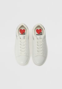 Sneaker in pelle bianca con finitura liscia, dotati di lacci e punta rotonda. Le sole interne presentano un design con un cuore rosso e la scritta "LOVE MOSCHINO."