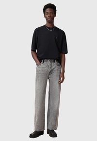 Black short-sleeve t-shirt, loose gray jeans with faded finish, and chunky black boots, presented on a model with hands in pockets.