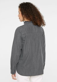 Gray button-up shirt with a ruffled collar, long sleeves, and gathered back detailing, made of a textured cotton-blend fabric.