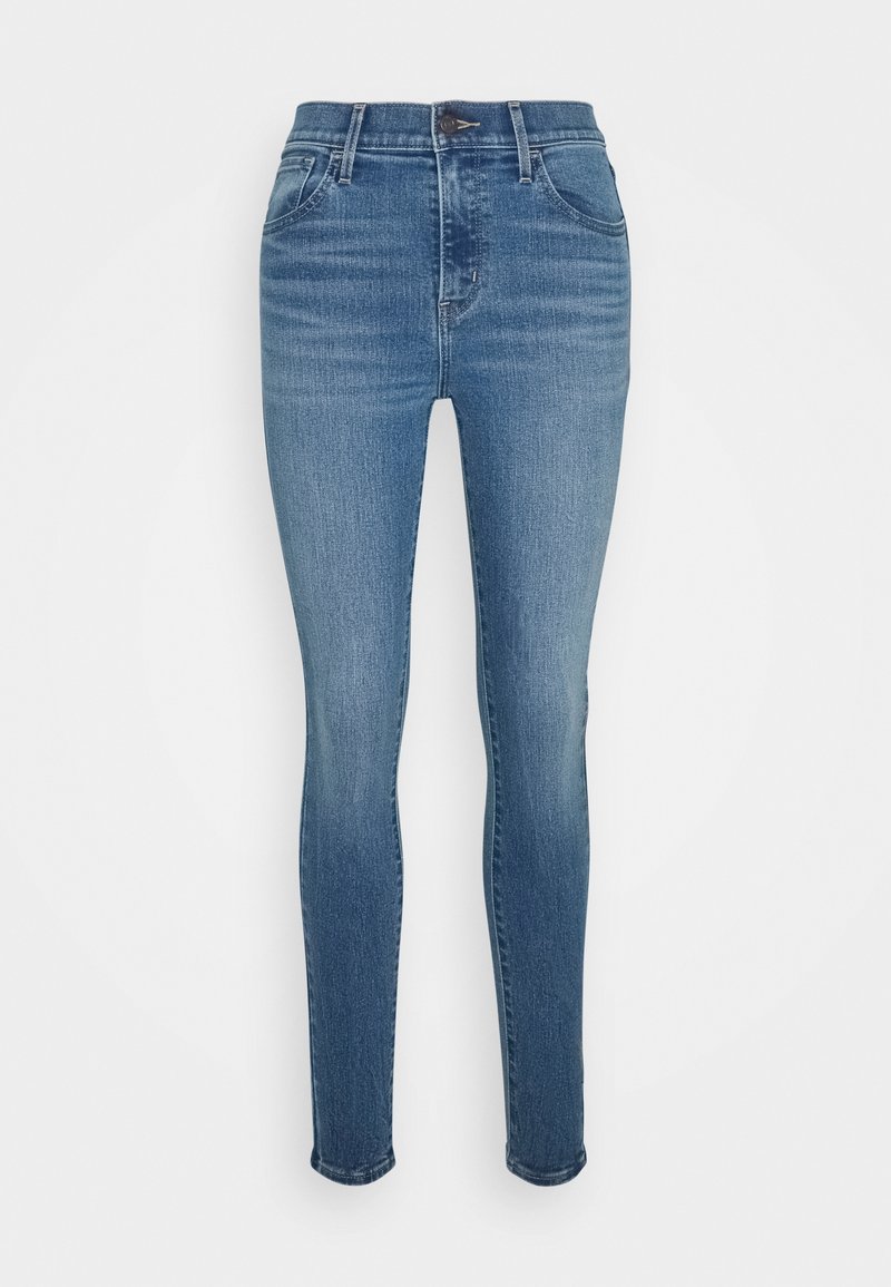 Jean skinny en denim bleu moyen, avec une taille haute, un design traditionnel à cinq poches et des détails de décoloration subtils sur l'ensemble du tissu.