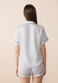 Ensemble de pyjama en satin bleu clair comprenant une chemise à manches courtes avec col et un short assorti ; les deux présentent des détails de piping noir.
