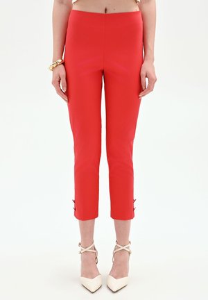 Pantaloni slim-fit rossi vivaci cropped con dettagli a bottoni vicino all'orlo, indossati con décolleté beige a punta con cinturini alla caviglia.