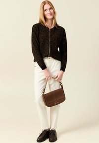 Brun leopardmönstrad zip-up tröja, krämfärgade tapered byxor, brun läderhandväska med randig axelrem och mörka skor. Neutral bakgrund.