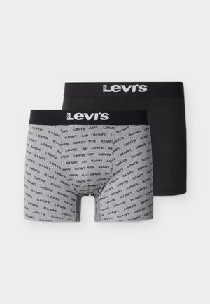 Jeune homme debout avec une expression neutre, portant un boxer gris de la marque Levi’s avec une ceinture noire.