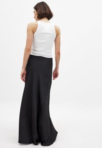 Schwarzer Satin-Maxirock mit einem ausgestellten Schnitt, kombiniert mit einem weißen, gerippten Tanktop, das eine glatte Textur und einen eleganten Fall zeigt.