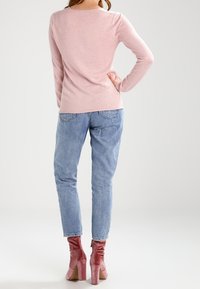 Jasnoróżowy sweter z długim rękawem o luźnym kroju, zestawiony z wyblakłymi niebieskimi jeansami i błyszczącymi różowymi botkami na grubym obcasie.