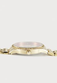 Guldtonet ur med en rund kasse, tekstureret bezel, pink urskive og et glat metalarmbånd. Inkluderer en sidekrone til justering af tiden.