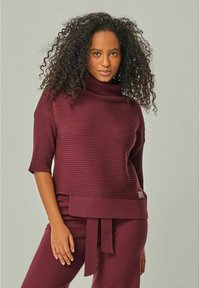 Burgunderfarbener Rippstrickpullover mit kurzen Ärmeln und hohem Rollkragen. Verfügt über eine gebundene Taille und strukturierte Details. Weiches, gemütliches Material.