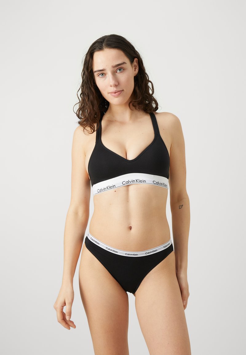 Zwarte katoenen bralette en bijpassende thong met een witte elastische band met het "Calvin Klein" logo. Glad materiaal, minimalistisch ontwerp.