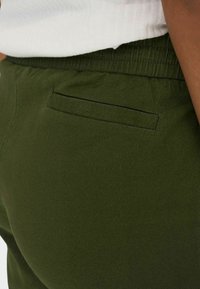 Zielone oliwkowe spodnie o gładkiej fakturze, z elastycznym pasem i tylną kieszenią z minimalistycznym klapkiem.