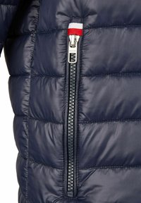 Navy Puffer-Jacke mit vertikalem Reißverschluss und silbernem Hardware sowie rot-, weiß- und blaufarbigen Akzenten am Kragen. Glatte, gestepfte Textur.