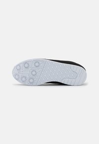 Černá podešev atletické obuvi s bílou gumovou spodní částí. Obsahuje kruhové vzory vzorku a texturované gripy pro lepší trakci.