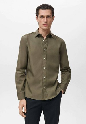 Olive green long-sleeve button-up shirt featuring a classic collar, smooth fabric, and a single chest pocket, paired with dark trousers.