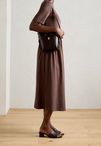 Personne portant une robe midi marron, des sandales à talons noires et un petit sac à bandoulière en cuir noir.