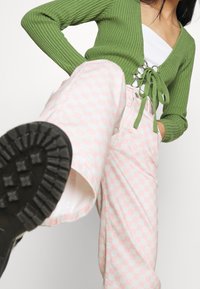 Zelený žebrovaný svetr s detaily na zavazování a stříbrným kováním; růžové a bílé kostkované kalhoty s vysokým pasem; černá texturovaná podrážka boty.