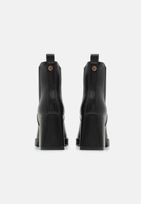 Bottines noires avec une finition en cuir lisse, talons blocs épais et une boucle pour un enfilage facile. Présente un logo embossé à l'arrière.