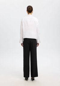 Witte longsleeve shirt met een standaardkraag, gecombineerd met zwarte wijde broek. Gladde stof, zichtbare knopen op de manchetten, minimalistisch ontwerp.