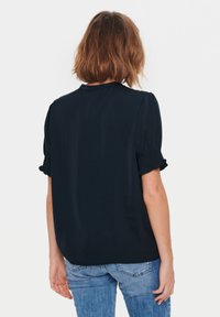 Blusa blu navy a maniche corte con scollatura tonda, maniche a sbuffo arricciate e una vestibilità comoda, abbinata a jeans azzurri chiari.