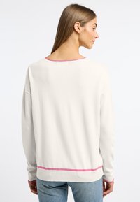 Witte trui met een ronde hals, roze afwerking bij de halslijn en zoom, lange mouwen, en een relaxte fit. Zachte textuur met een gladde afwerking.