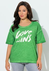 Grünes T-Shirt mit kurzen Ärmeln und rundem Ausschnitt, vorne mit weißem Textgrafik "LOVE WINS". Weicher, strukturierter Stoff.