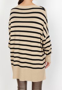 Beige oversized trui met zwarte horizontale strepen, geribde manchetten en een relaxte pasvorm. Zachte textuur met een ronde halslijn.