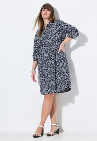 Abito camicia a stampa floreale in blu navy e bianco, con bottoni frontali, maniche 3/4, tasche laterali e vestibilità comoda. Abbinato a sandali con tacco a blocco.