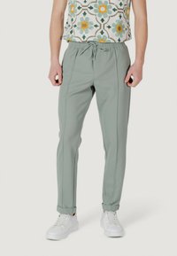 Pantaloni della tuta verde chiaro con vita elastica e cordoncino, caratterizzati da cuciture laterali e caviglie a costine, abbinati a sneakers bianche.